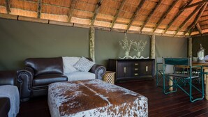Una habitación acogedora con un sofá de cuero, un cojín decorativo estampado, un armario de madera y un rincón comedor con mesa y sillas.
