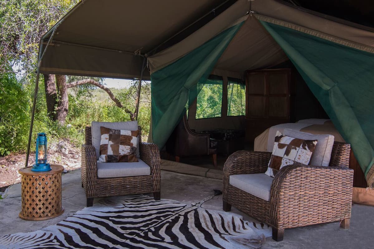 A tented accommodation with wicker furniture, a zebra rug, and a lantern.