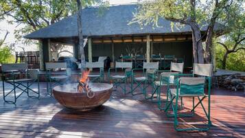 An outdoor seating area with a fire pit, green chairs, and a covered dining area with tables and chairs.