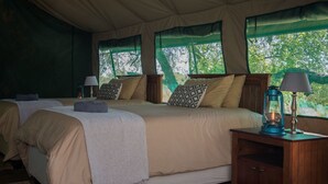 Alojamiento con carpa que incluye dos camas, cada una con cabecero de madera, una mesita de noche con lámpara y vistas a la vegetación.