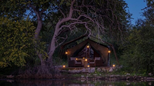 Una cabaña acogedora junto a un lago al anochecer, con chimenea de piedra y zona de comedor.