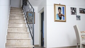 A staircase with a metal railing, a framed portrait on the wall, and a chair with a floral cushion. - BFAME - Cornice Barocca (Ragusa)