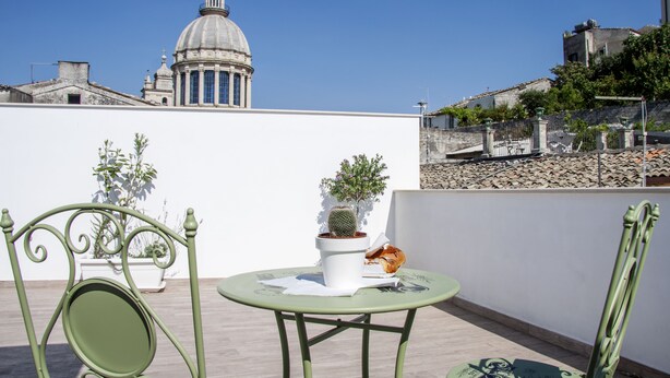 A rooftop terrace with a table and chairs, potted plants, and a view of a historic building with a dome. - BFAME - Cornice Barocca (Ragusa)