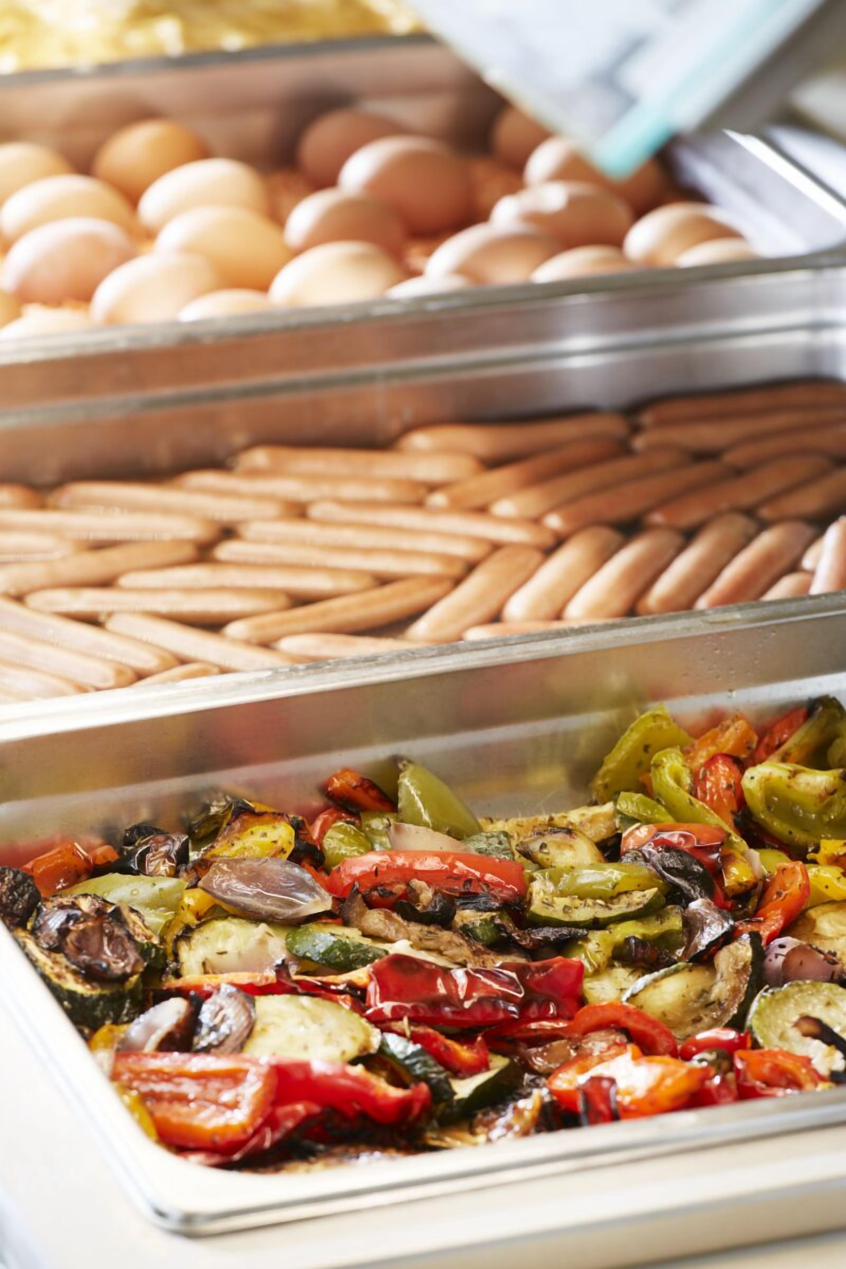 A buffet with various food options including eggs, sausages, and roasted vegetables.