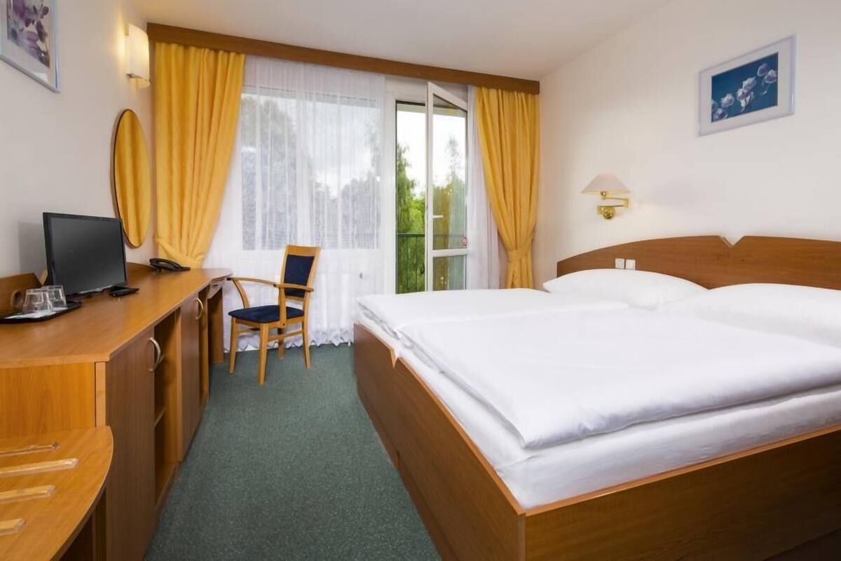Ein Hotelzimmer mit Bett, Schreibtisch, Stuhl und einem fenster mit Vorhängen.