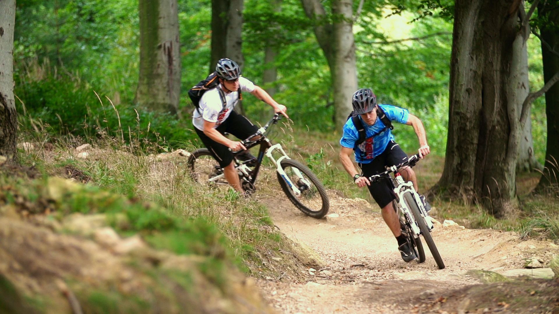 Dos ciclistas de montaña en un sendero de tierra rodeado de árboles.