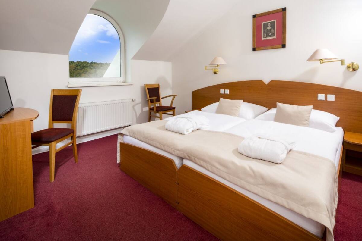 Ein Hotelzimmer mit einem großen Bett, zwei Sesseln, einem Schreibtisch, einem Fenster mit Blick und einem gerahmten Bild an der Wand.