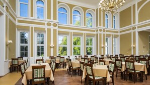 Une grande salle à manger avec de nombreuses tables et chaises, de hauts plafonds et de grandes fenêtres.