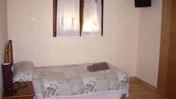 A small bedroom with a bed, a wooden nightstand, a window with curtains, and a wall-mounted TV.