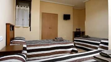 A room with two beds, a wooden wardrobe, a television on the wall, and a door.