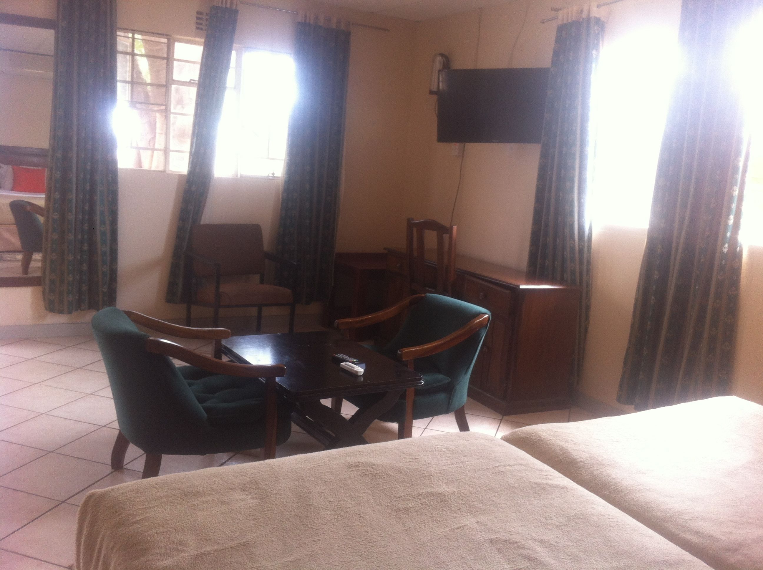 A hotel room with two beds, a small table, two chairs, a TV on the wall, and curtains on the windows.