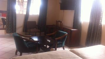 A hotel room with two beds, a small table, two chairs, a TV on the wall, and curtains on the windows.