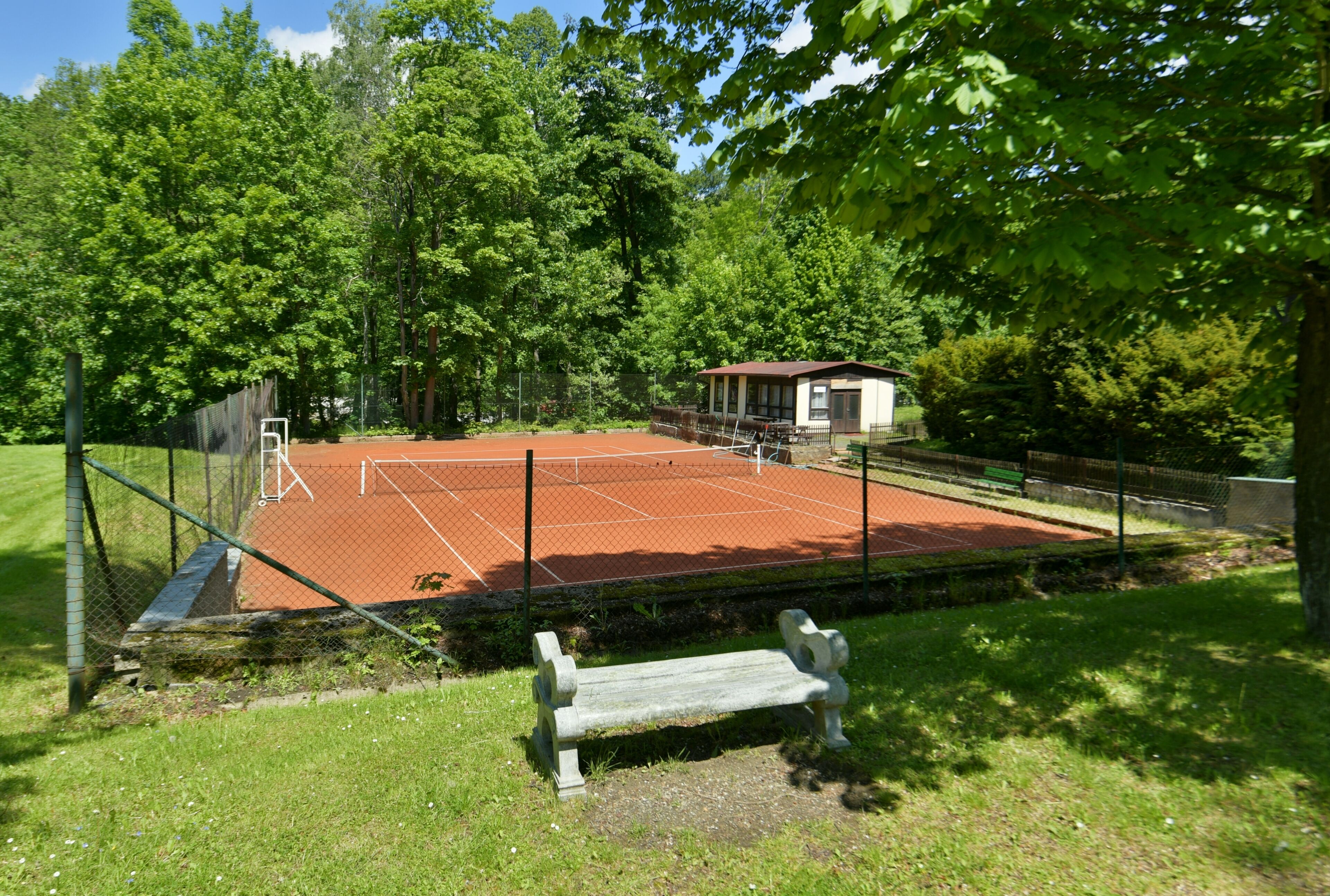 A tennis court surrounded by trees, a bench, and a small building.