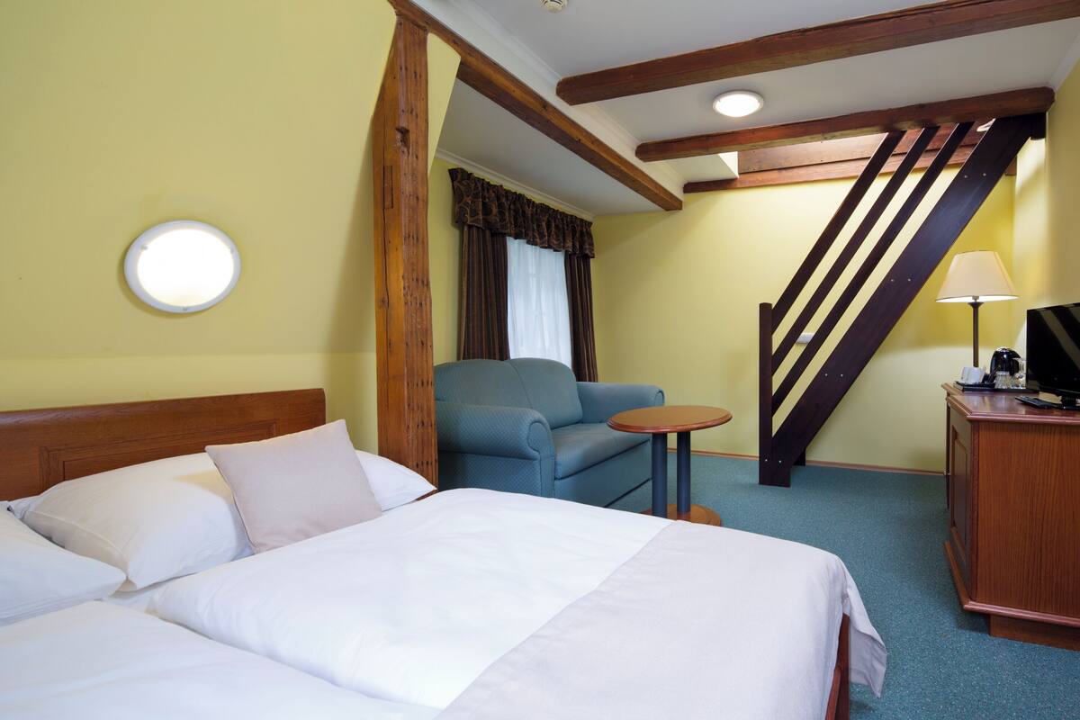 A hotel room with a large bed, a small table, a chair, a desk, and a staircase.