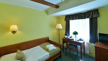 A hotel room with a bed, desk, chair, lamp, TV, and window with curtains.