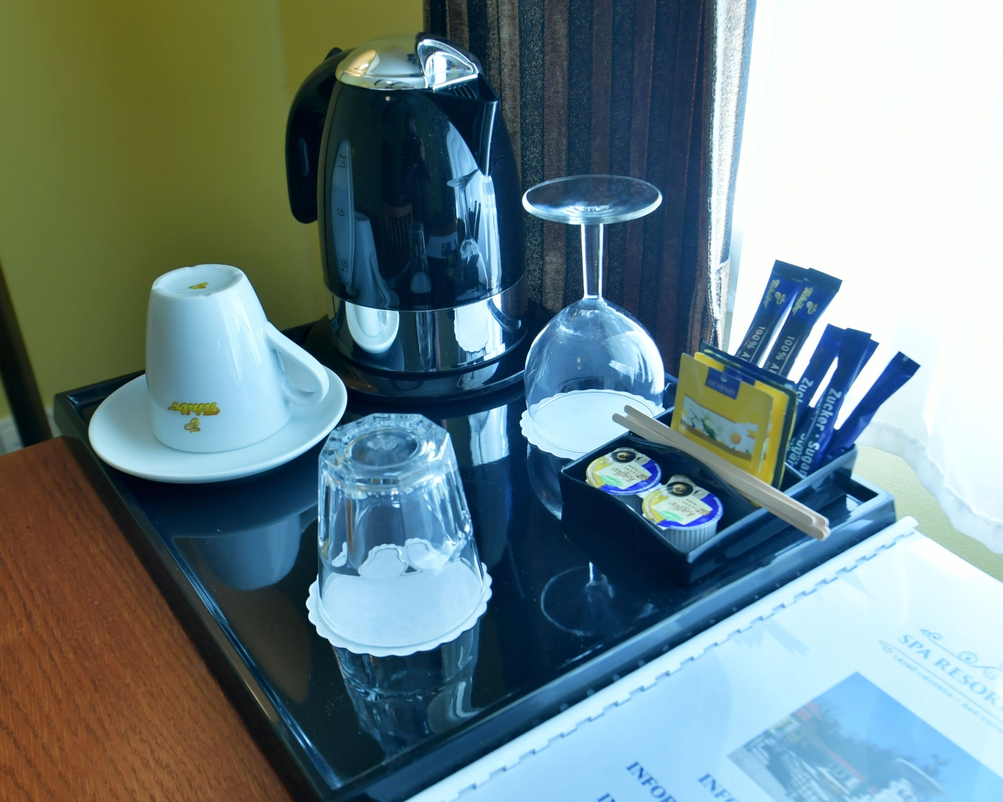 Un plateau avec une cafetière, une tasse blanche, un verre, un verre à vin et quelques collations emballées.