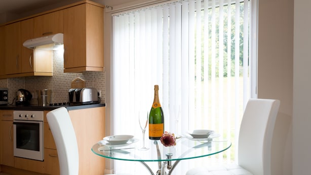 Una cocina moderna con armarios de madera, una mesa de vidrio, sillas blancas y una botella de champán sobre la mesa.