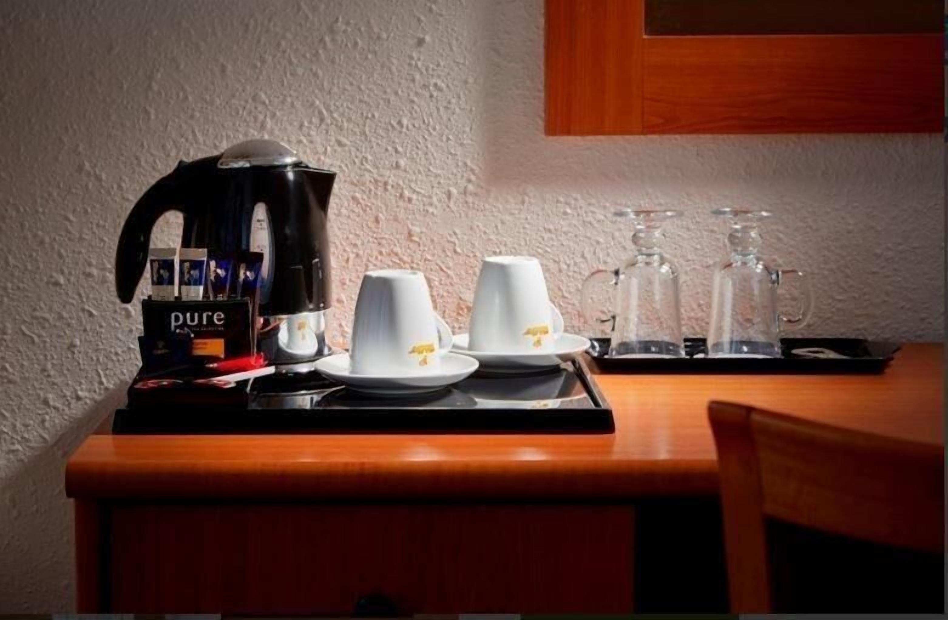 A coffee station with a coffee maker, cups, and glasses on a tray.