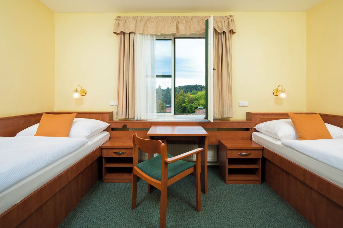 A hotel room with two single beds, a wooden desk, a chair, and a window with curtains.
