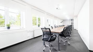 A conference room with a long table, black chairs, and large windows with plants.