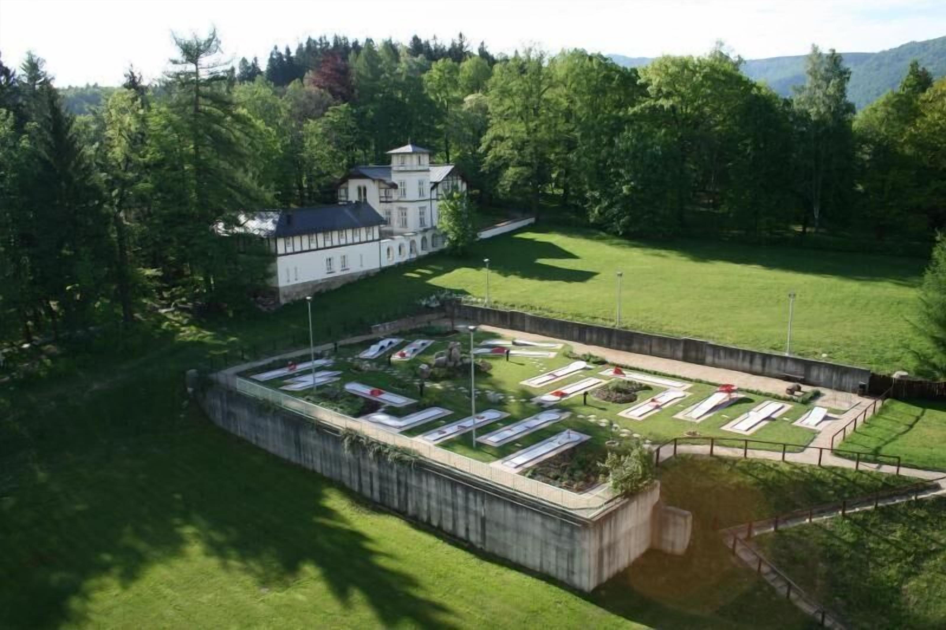 A large, rectangular building with a symmetrical facade and a central tower, surrounded by a well-maintained lawn and a small pond.