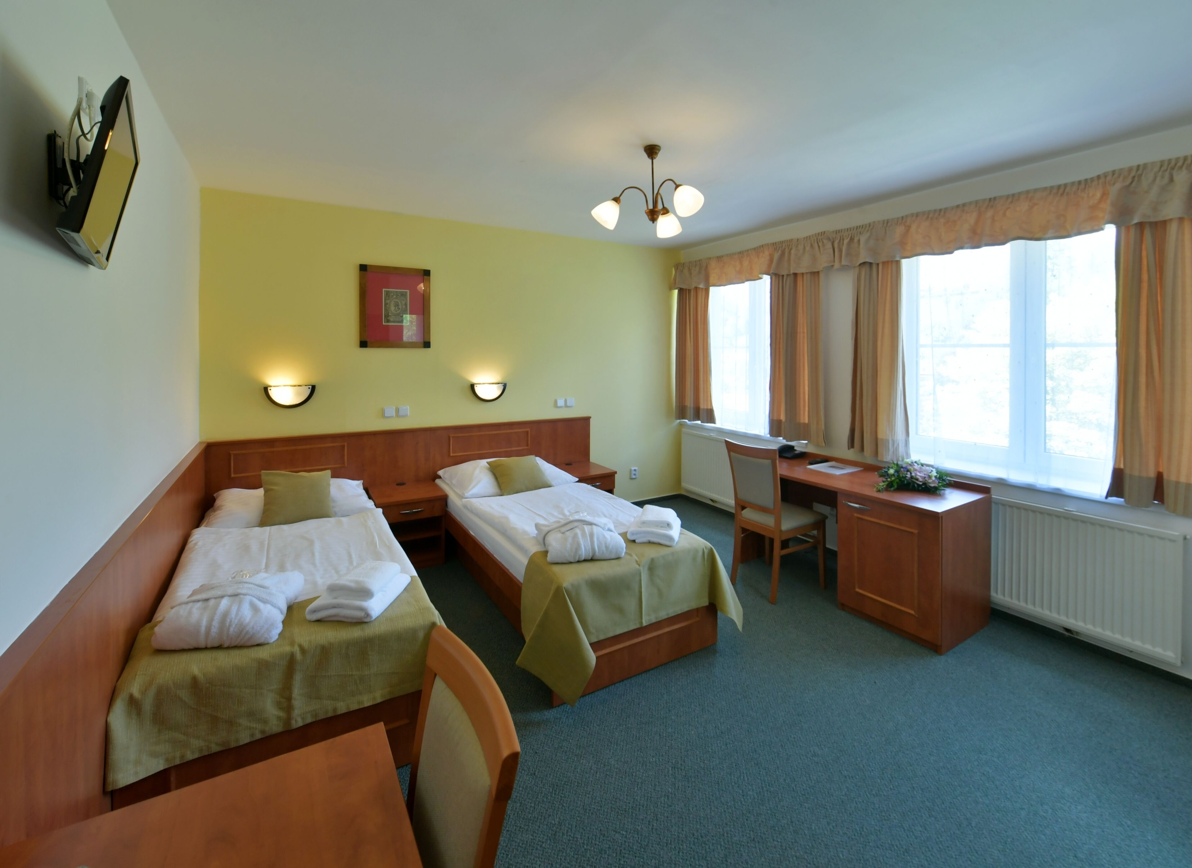 A hotel room with two single beds, a desk, a chair, and a radiator.
