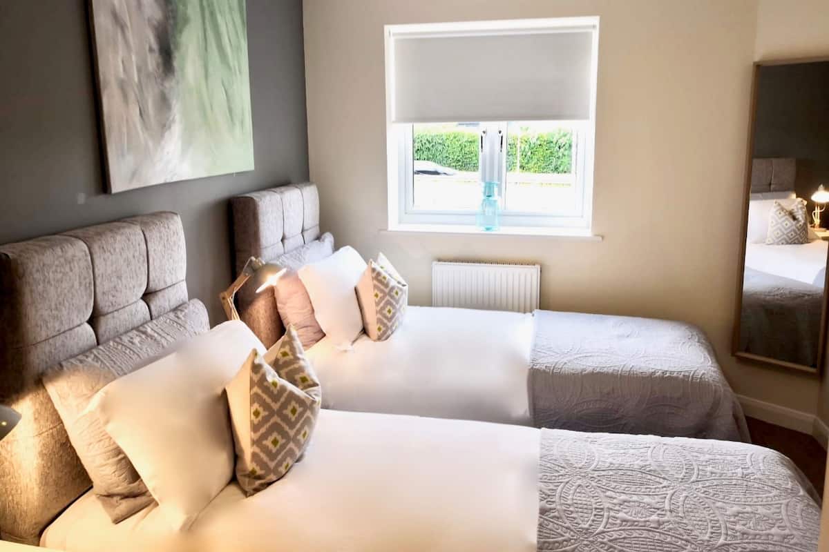 A hotel room with two beds, a large window, a radiator, and a painting on the wall.