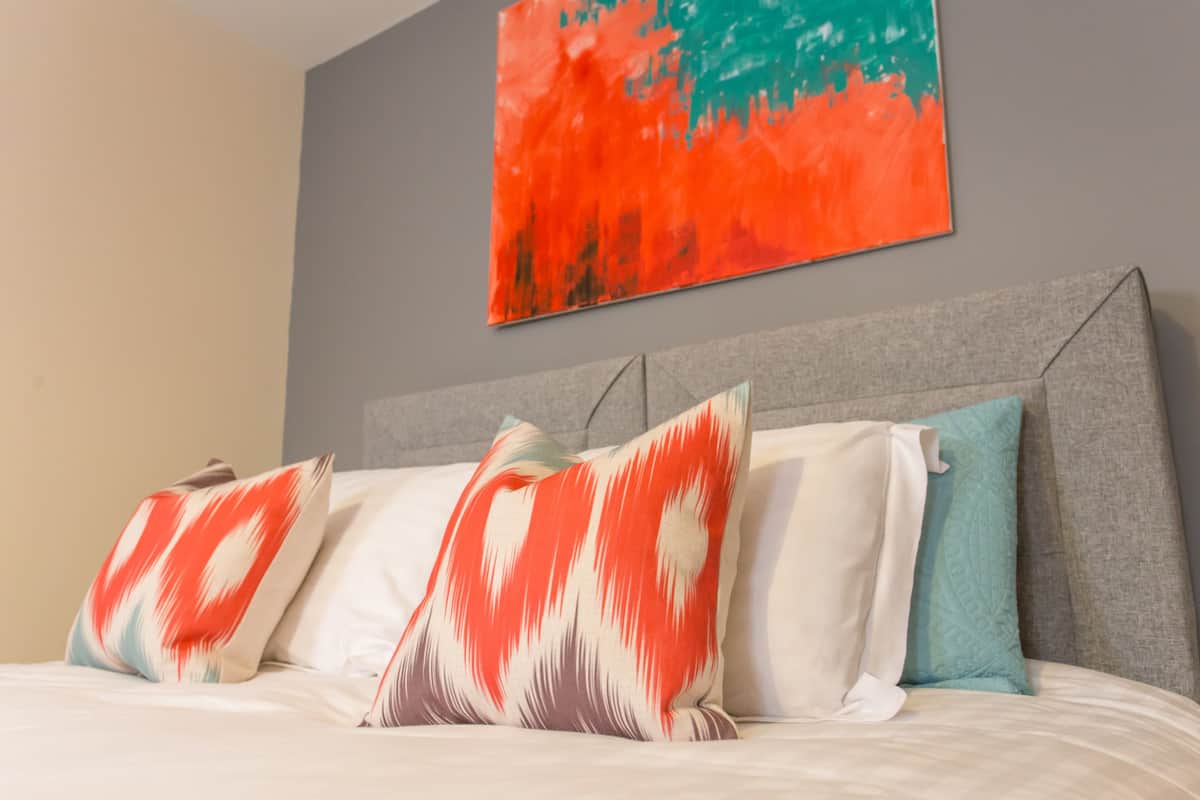 A bed with multiple pillows and a painting on the wall.