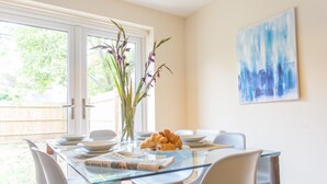A dining area with a glass table, chairs, a vase with flowers, and a painting on the wall. - Razia Apartments (Oxford)