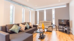 A modern living room with a sofa, armchair, and a glass coffee table with books and a lamp. - Razia Apartments (Oxford)