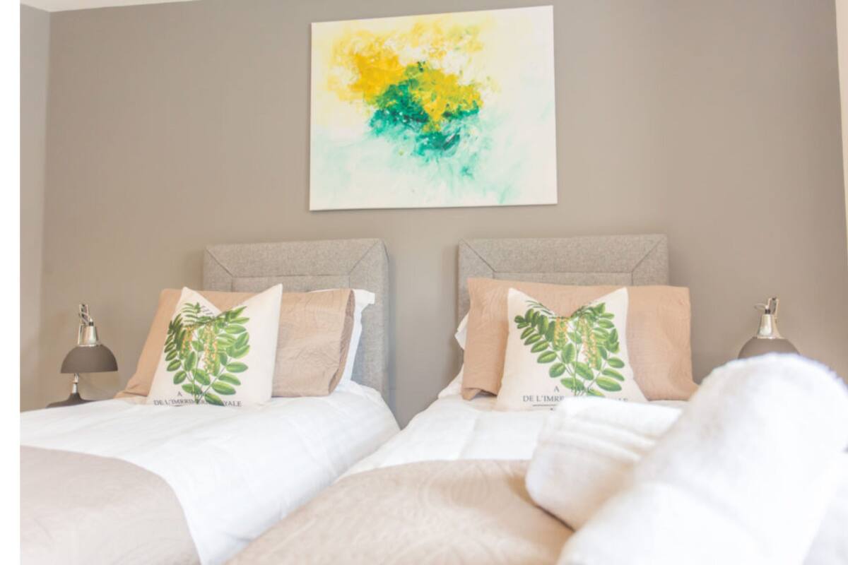 A hotel room with two beds, each with a headboard and pillows featuring a green leaf design.