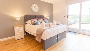 A bedroom with a bed, bedside tables, a wall-mounted light fixture, and a large window. - Razia Apartments (Oxford)