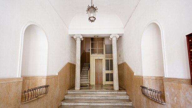 Eine imposante Treppe mit weißen Säulen und Holzvertäfelung, die zu einer Tür mit Glasscheiben führt.