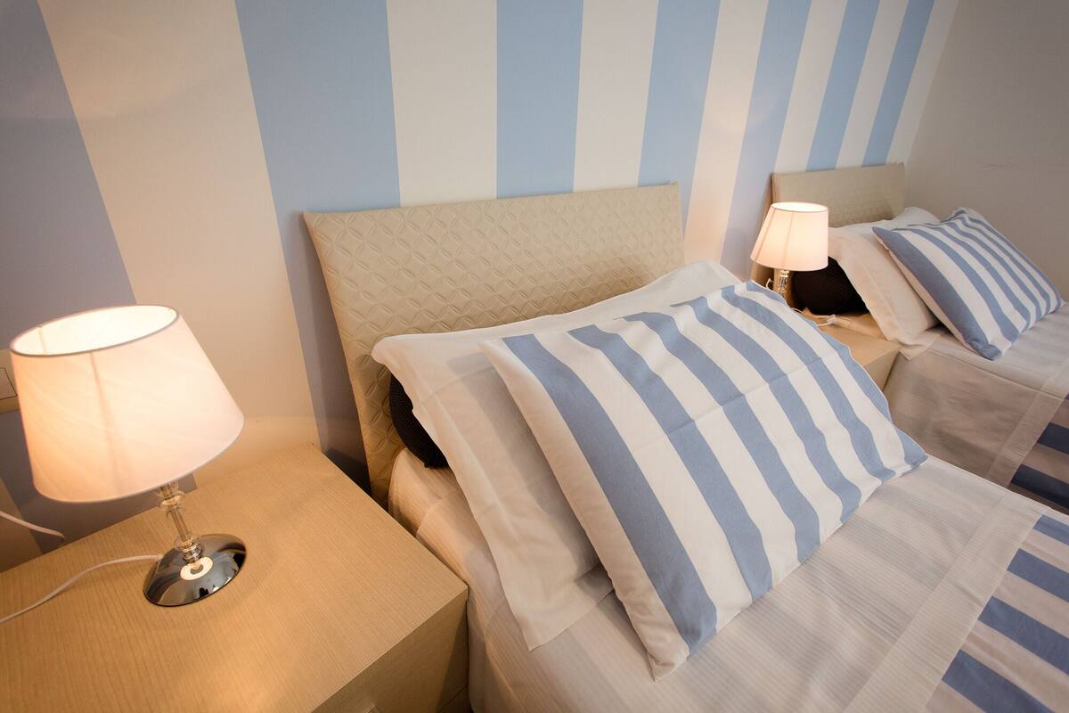 Una habitación de hotel con una pared a rayas, dos mesitas de noche con lámparas y una cama con ropa de cama a rayas.