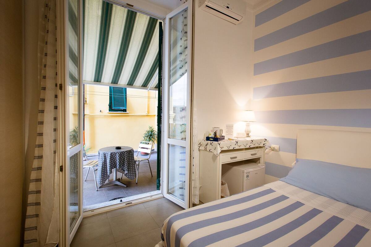 Habitación de hotel con cama, escritorio con lámpara, una silla y vista al balcón exterior.