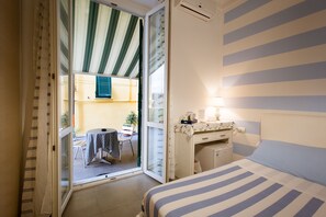 Et hotelværelse med seng, skrivebord med lampe, stol og udsigt til altanen.