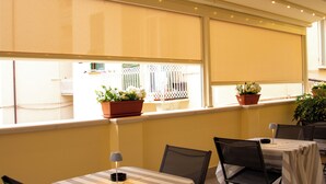 Ein Restaurant mit Tischen, die mit gestreiften Tischdecken bedeckt sind, Stühlen und Blumentöpfen auf der Fensterbank.