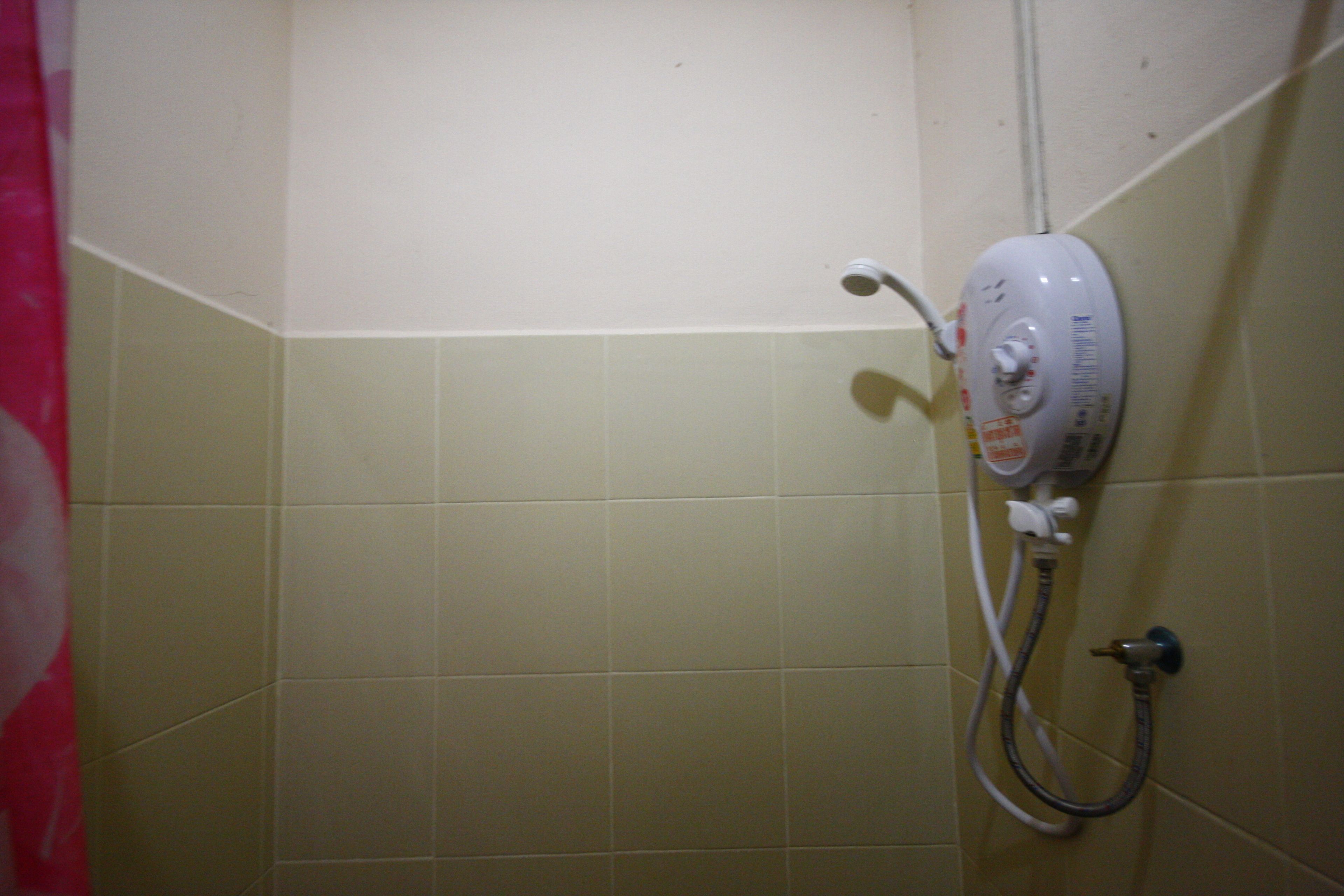 Un baño con azulejos color beige, un cabezal de ducha y un rociador de mano.