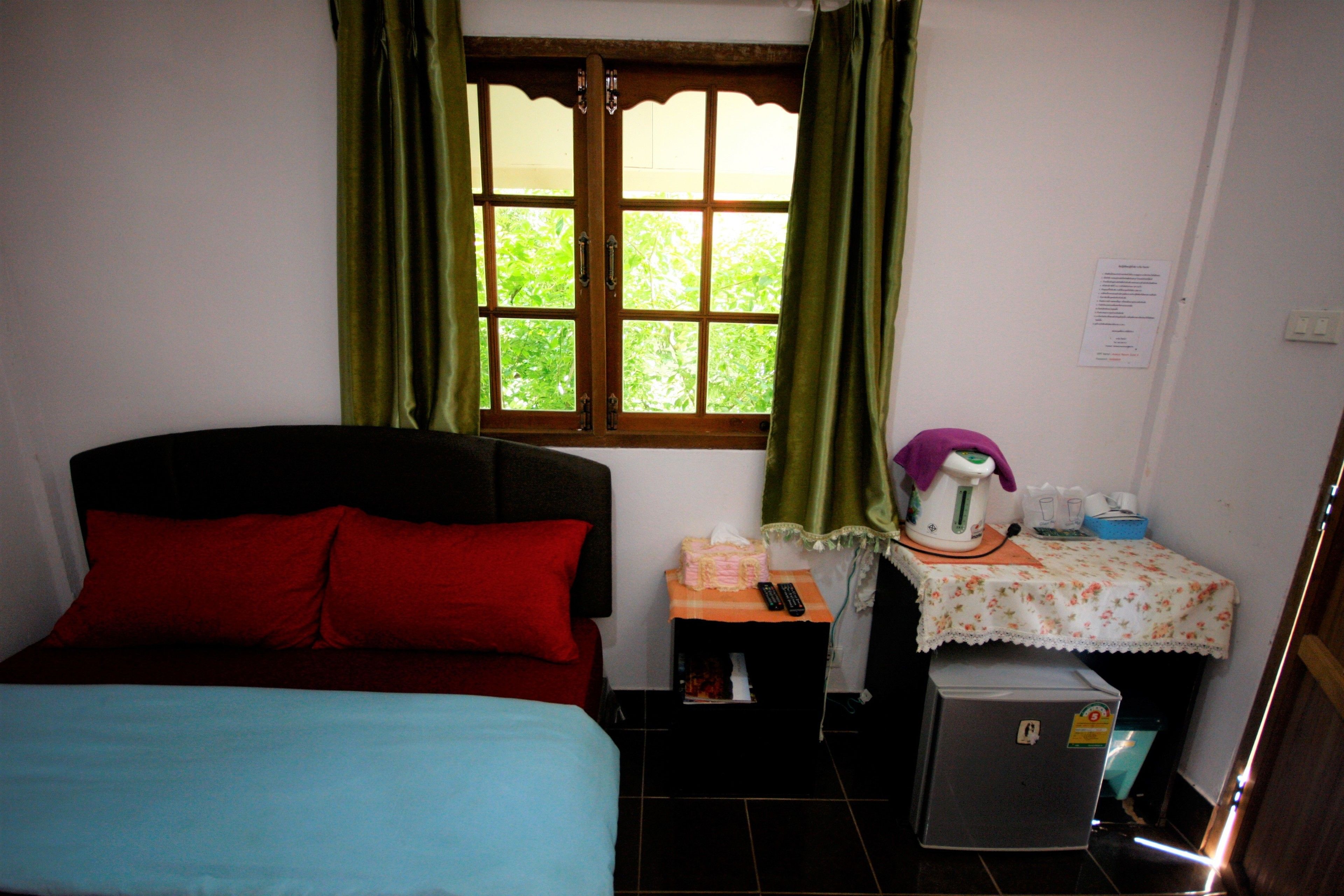 A small room with a bed, a table with a kettle, and a refrigerator.