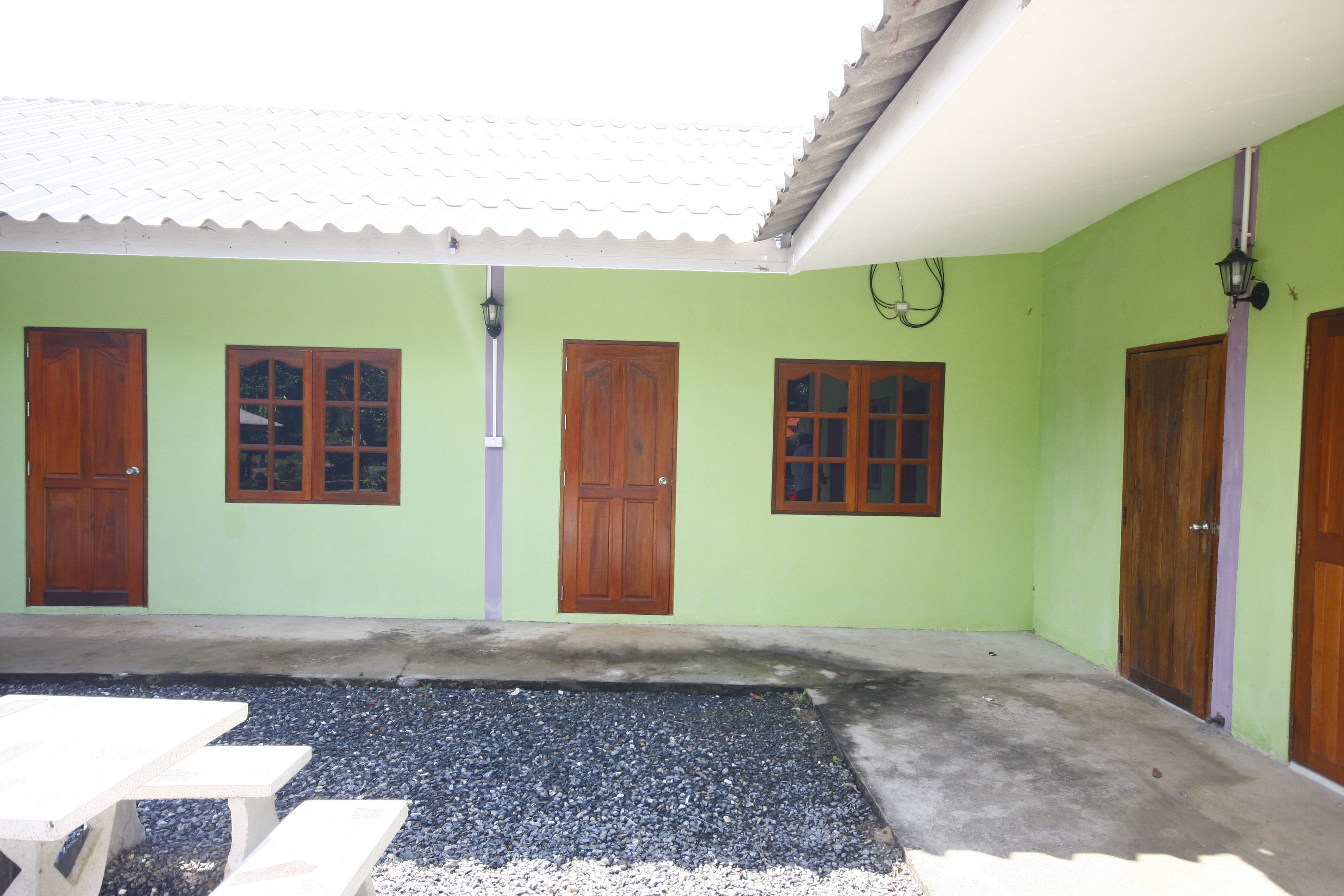 Un patio con un muro verde, tres puertas de madera y un suelo de hormigón.