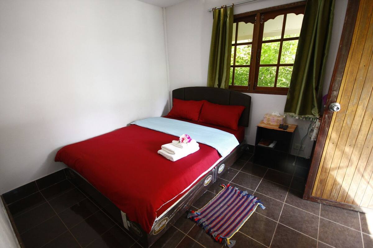Una cama con ropa de cama roja, una manta azul y una toalla blanca con un estampado floral.