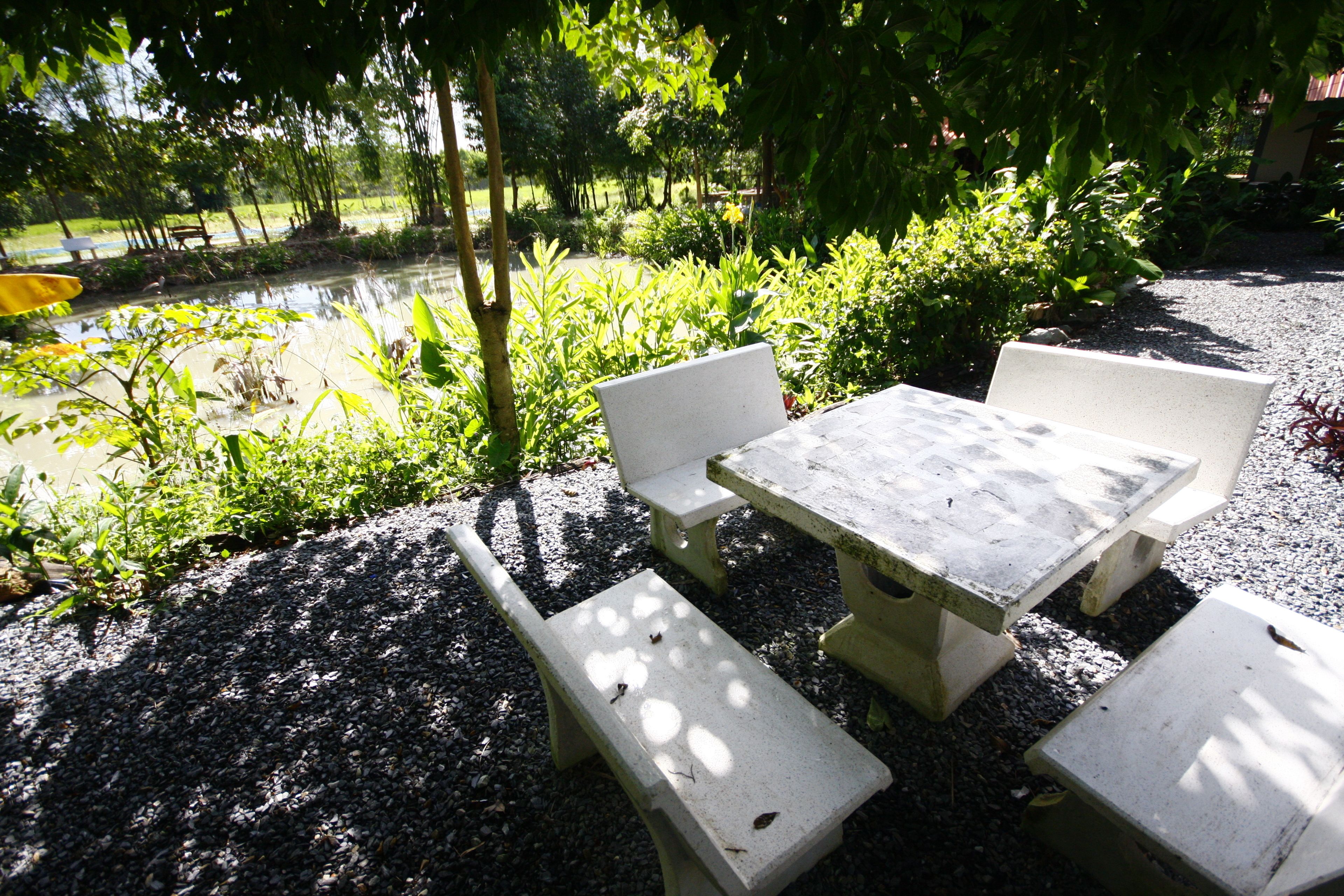 A concrete outdoor table and benches in a garden area with gravel ground, surrounded by greenery and trees.