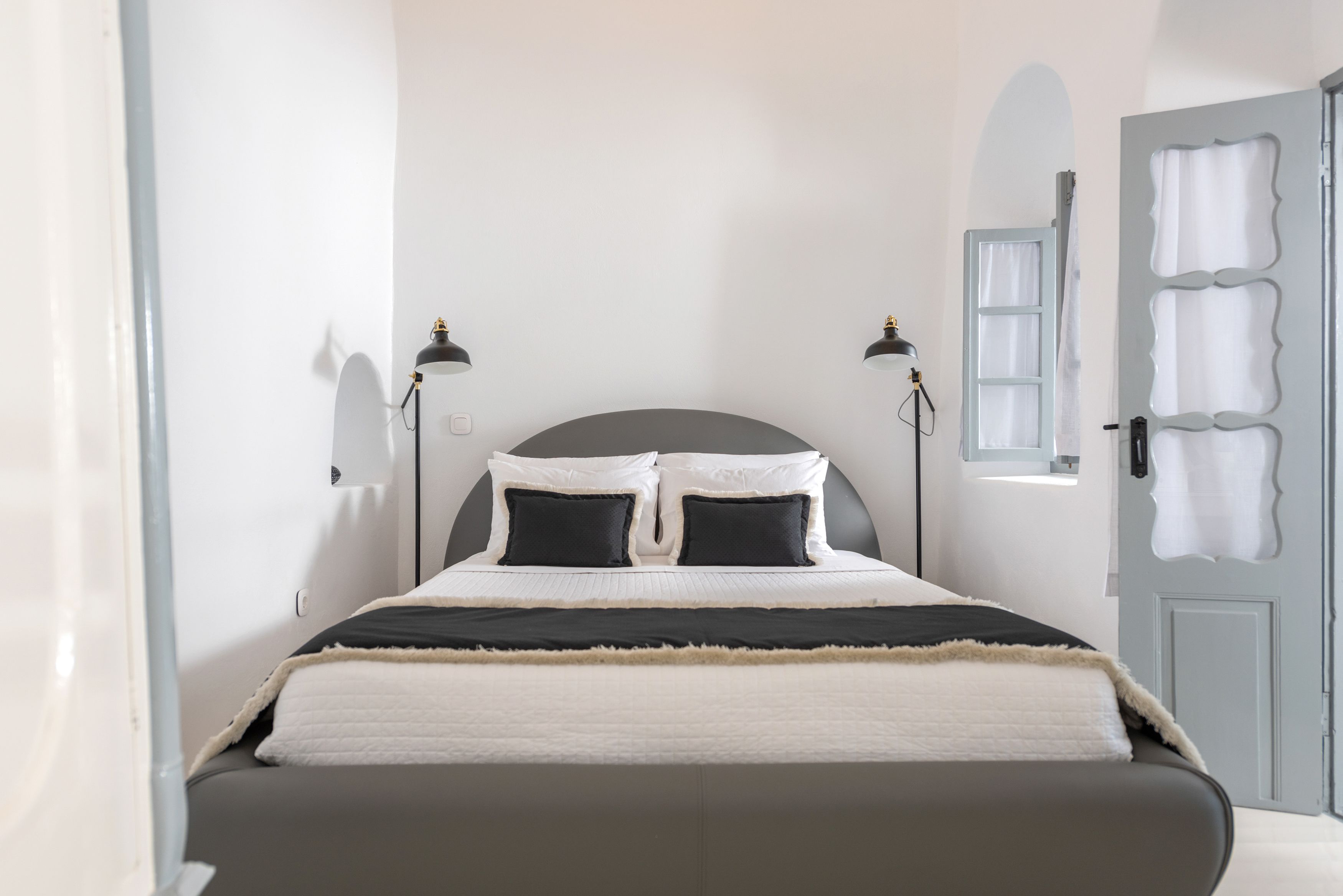 Ein ordentlich eingerichtetes Schlafzimmer mit Bett, Nachttischlampen und einer Tür mit Zierverkleidung.