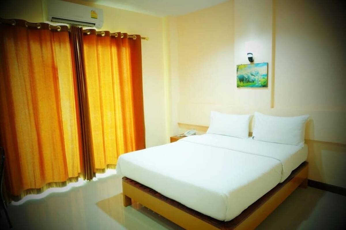 Een hotelkamer met een bed, gordijnen, een schilderij en een nachtkastje.