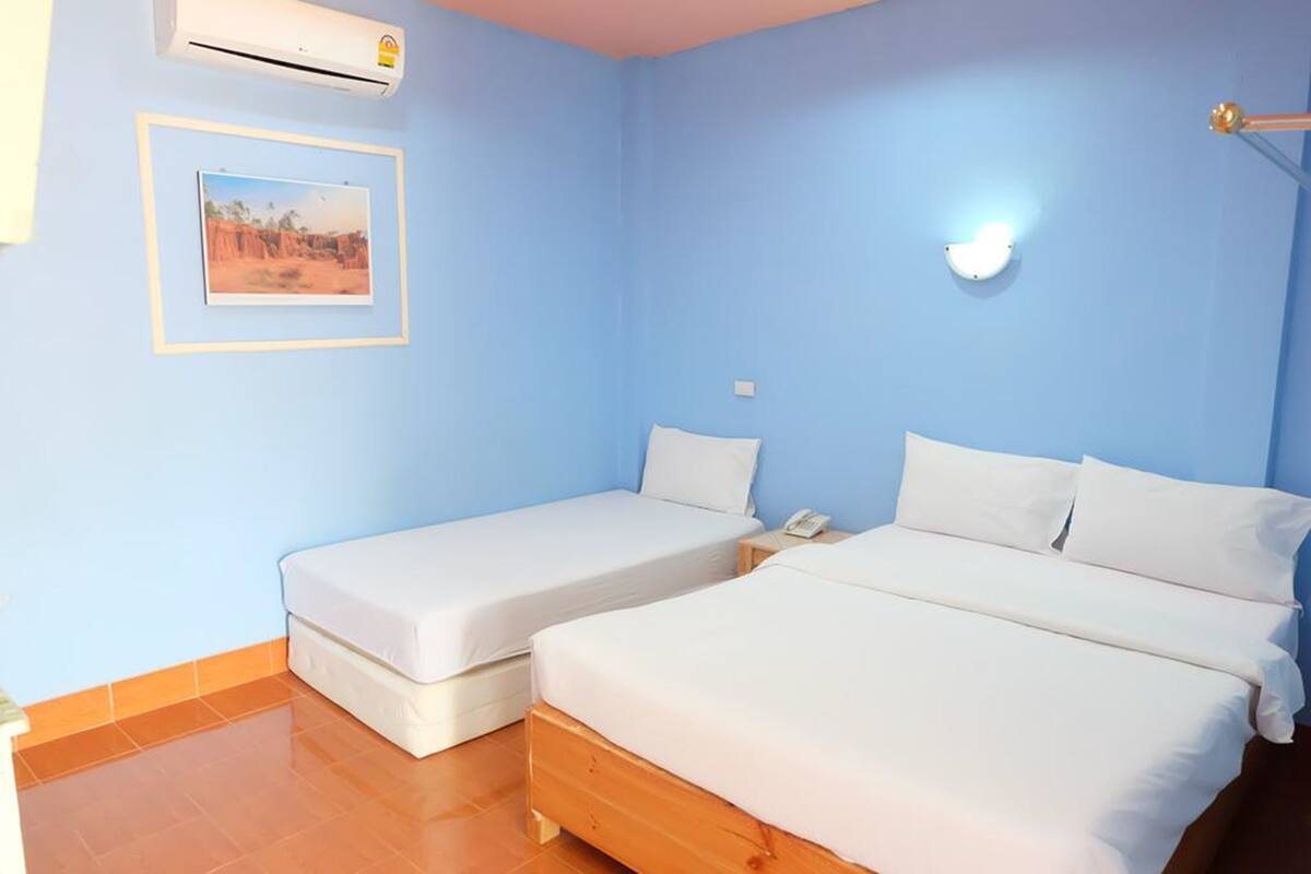 Een kamer met twee bedden, een wandairconditioner, een lijst met een afbeelding en een bedlampje.