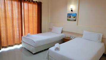 A hotel room with two single beds, a nightstand with a phone, a painting on the wall, and a window with curtains.