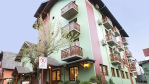 A multi-story building with balconies, a sign indicating no parking, and a restaurant with outdoor seating. - Pousada Belluno (Gramado)