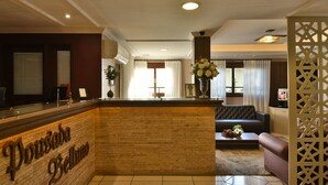 A reception area with a reception desk, a sofa, and a decorative partition. - Pousada Belluno (Gramado)