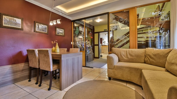 A living room with a sofa, a dining table with chairs, and a glass door leading to a staircase. - Pousada Belluno (Gramado)