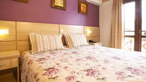 A bedroom with a floral bedspread, a wooden headboard, and two wall-mounted lamps. - Pousada Belluno (Gramado)